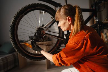 Evde bisiklet tamir eden orta yaşlı bir kadının portresi. Bisikletinin arka raydan çıkmasını ayarlayan kadın bisikletçi. Boşluğu kopyala
