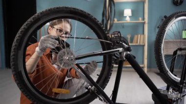 Evde bisiklet tamir eden bir kadın odada tekerlek zincirini inceliyor. Boşluğu kopyala