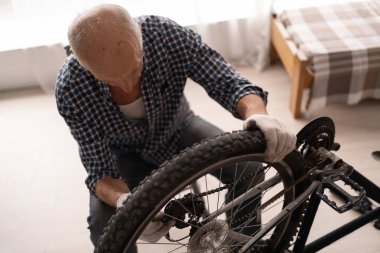 Yaşlı kel adam evde bisikletini tamir ediyor. Bisiklet tamiri ve bakım konsepti. Yeni yaz sezonuna hazırlanıyorum. Üst görünüm