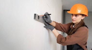 Kadın mühendis ya da mimar koruyucu bir miğferin duvar ölçüsünü ölçer. Evdeki bir inşaatçı beton bir duvarı kontrol ediyor. Onarım ve inşaat konsepti.