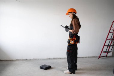 Turuncu kasketli mimar elinde bir pano tutuyor ve inşaat alanında duruyor. Bina teftişi, mimari planlama, inşaat denetimi ve mesleki rol kavramı.