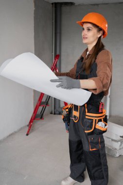 Tamamlanmamış binanın içinde el çizimi proje planı tutan kadın inşaat işçisinin portresi. Kadın inşaat mesleği, planlama aşaması, sanayi bölgesi ve profesyonel çizim kavramı.