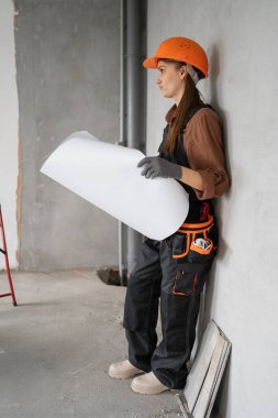 Miğferli ve tulumlu inşaat işçisi inşaat ve yenileme sırasında yeni evin planlarını okuyor. Boşluğu kopyala