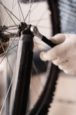 Bisiklet tamir atölyesinde çalışan erkek tamircinin yakın çekimi. Özel bir aletle bisikleti tamir ediyor. Boşluğu kopyala