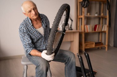 Oturma odasındaki sandalyede oturan bisiklet tekerini tamir eden yaşlı tamirci. Bisiklet onarımı ve bakım konsepti