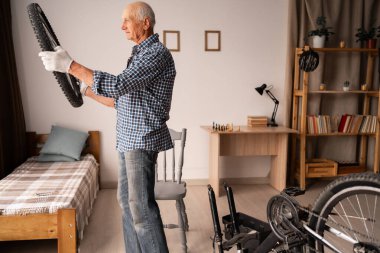 Yaşlı adamın arka tekerlek ayarlaması. Evde çalışan yaşlı bir tamirci bisikletini tamir ediyor. Pankart. Boşluğu kopyala