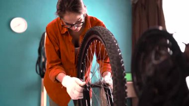 Gözlüklü bir kadın bisiklet tekerleği monte ediyor, evde bisiklet bakım servisi yapmak için onu söküyor. Boşluğu kopyala