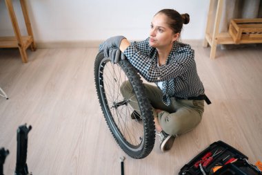 Yorgun kadın bisikletçi lastik bakım rutinini kontrol ediyor. Spor bir kadın hasar görmüş bisiklet tekerini inceliyor. Evde bisiklet tamir ediyor. Boşluğu kopyala