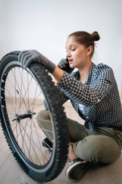 Aktif kadın bisikletçi lastik bakım rutinini kontrol ediyor. Zarar görmüş bisiklet tekerini inceleyen sportif kadın akıllı telefon kullanarak arıyor.