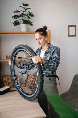 Bisiklet tekerleği test eden masanın yanında duran genç bir kadın. Evde motoru tamir ediyor. Boşluğu kopyala