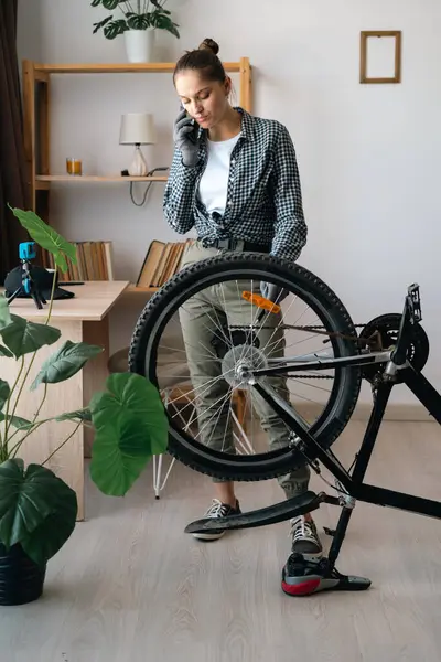 Evde bozuk bisikleti tamir ederken teknisyen ya da tamirciyle cep telefonunda konuşan bir kadın. Boşluğu kopyala