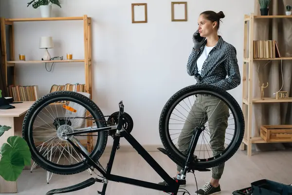 Evde bozuk bisikleti tamir ederken teknisyen ya da tamirciyle cep telefonunda konuşan bir kadın. Boşluğu kopyala