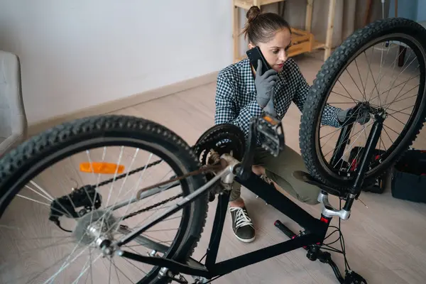 Evde bozuk bisikleti tamir ederken teknisyen ya da tamirciyle cep telefonunda konuşan bir kadın. Boşluğu kopyala