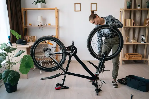 Dişi bisikletçi, bisikletle evde. Bisiklet parçaları tutan teknisyen, kamerada tamir yapıyor. Boşluğu kopyala