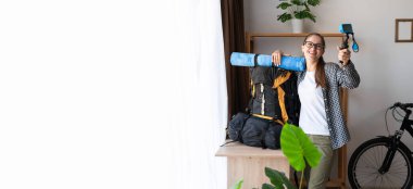 Genç bir kadın yürüyüşçü, elinde büyük bir sırt çantasıyla evde bir kamera ile geziye çıkıyor. Pankart. Boşluğu kopyala