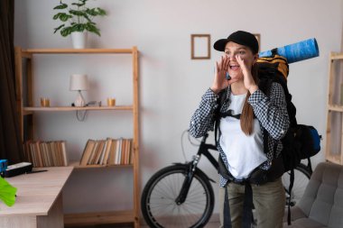Genç bayan yürüyüşçü evde bağırarak sırt çantasıyla gezmeye hazır, pozitif ruh hali. Ticari reklam konsepti. Boşluğu kopyala
