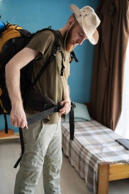 Genç sakallı gezgin evde büyük bir sırt çantası yürütmeye hazırlanıyor. Sırt çantalı seyahat konsepti. Boşluğu kopyala