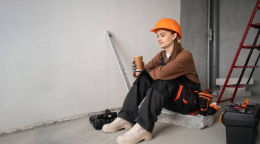 Tamirci ya da miğferli bir tamirci inşaat alanında kahve molası veriyor, evin tadilatı sırasında dinleniyor, üniforma giyiyor, dinlenme sembolü, iş dengesi, tamir konsepti, yaşam tarzı...