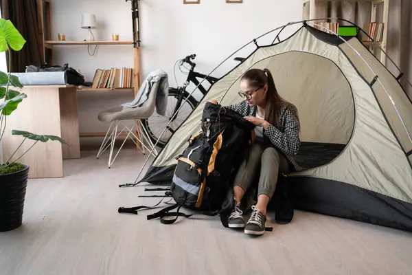 Gözlüklü ve günlük kıyafetleriyle sırt çantasıyla çadırda oturan sırt çantalı bir kadın eve dönüş yolculuğuna hazırlanıyor.