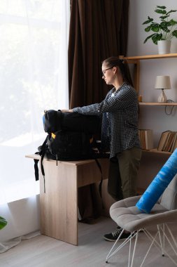 Dağ yürüyüşü için hazırlanan bayan yürüyüşçü evinin oturma odasında sırt çantası ve ekipman hazırlıyor. Boşluğu kopyala