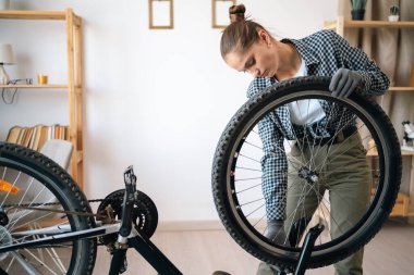 Evde bisikletini tamir eden ve ona bakan genç bir kadın. Boşluğu kopyala