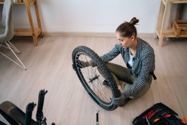 Bisikletinin tekerini tamir eden genç bir kadın evde yerde oturuyor. Boşluğu kopyala