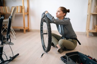 Bisikletinin tekerini tamir eden genç bir kadın evde yerde oturuyor. Boşluğu kopyala