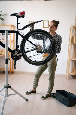 Bisikletli kadın tamirci evde tamir standında bisiklet tamir ediyor. Boşluğu kopyala