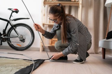 Woman assembling tent at home. Adventure, camping, and exploration. Copy space