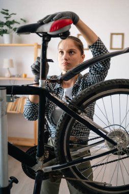 Female biker assembling and securing bicycle seat at home, concept of DIY repair, active leisure and hands-on hobby, maintaining and adjusting bike parts indoors