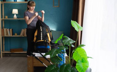 Orta yaşlı bayan yürüyüşçü evdeki oturma odasında yürüyüş yapmak için sırt çantası hazırlıyor. Seyahat, turizm ve yürüyüş konsepti