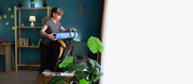 middle aged woman standing at home packing hiking backpack with equipment and clothes for mountain trip, preparing for journey, tourism, trekking, hiking and adventure planning