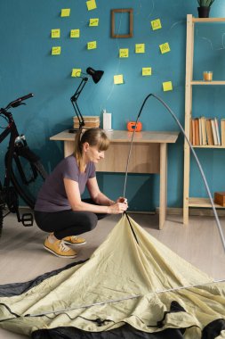 Woman assembling camping tent at home preparing for hike. Trip preparation concept