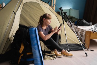 Orta yaşlı bir kadın çadırın yanında oturmuş evdeki akıllı telefonu kullanıyor. Turist aktif bir hayat sürüyor. Yürüyüş, seyahat ve gezi konsepti