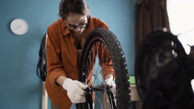 Genç bir kadın yeni sezon için bisikletini tamir ediyor. Bisiklet tekerleği evde. Boşluğu kopyala