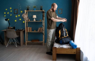 Sırt çantalı genç yürüyüşçü evdeki yatak odasında geziye hazırlanıyor. Boşluğu kopyala