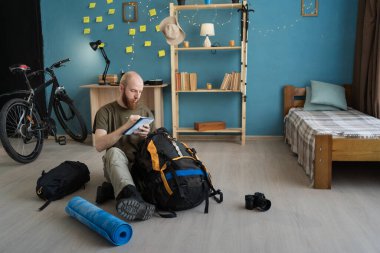 Sakallı gezgin, kamp malzemelerini toplamaya hazırlanıyor. Sırt çantası, uyku tulumu ve seyahat için uyku tulumu. Boşluğu kopyala