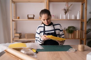 Kadın evde balmumu çarşafları kullanarak el yapımı mumlar yapmaya hazırlanıyor, rahat atölyede çevre dostu diy aktivitesi, doğal malzemeler, hobi konsepti, yaratıcı küçük işletme fikri