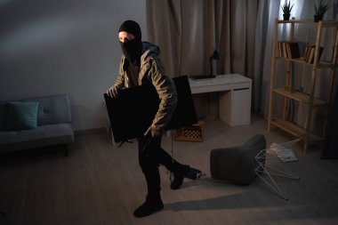 Siyah kar maskeli bir adam evden televizyon çalıyor. Maskeli yüz. Hırsız televizyon çalıyor. Boşluğu kopyala