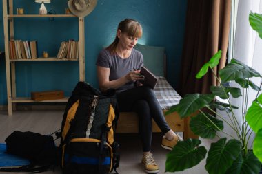 Üst düzey bir kadın bir kontrol listesi ile seyahat planlıyor sırt çantası için hazırlık yapıyor. Seyahat, planlama ve yürüyüş konsepti