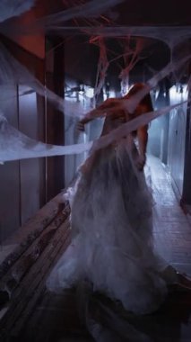 Gelinlikli Ölü Kadın Gelini, kameraya bakan örümcek ağlarıyla koridorda yürürken görülüyor. Uzayı kopyala Arka plan