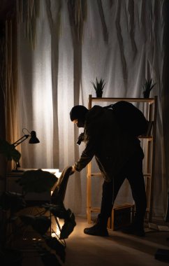 Hırsız ya da davetsiz misafir evin içinde el feneriyle para arıyor. Siyah kar maskeli bir hırsız. Boşluğu kopyala