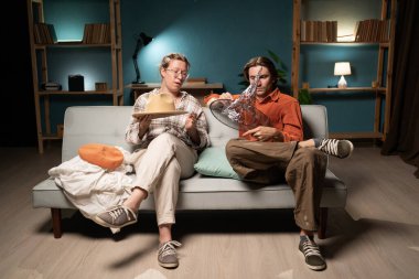 Akşam oturma odasında kanepede oturan erkek ve kadın Cadılar Bayramı kostümleri için değişik komik şapkalar deniyorlar evde yapılacak partiye hazırlanıyorlar. Mutlu Cadılar Bayramı kutlamaları. Sıcak atmosfer.