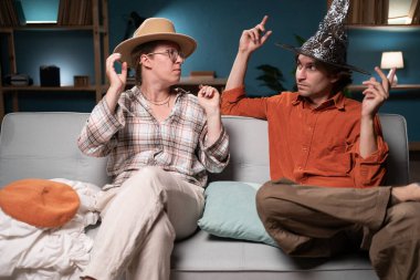 Oturma odasındaki kanepede oturan aile çifti farklı şapkalar deniyor, akşam için kostüm partisi hazırlıyorlar. İlişki kavramı, eğlence, birliktelik, mizah ve kutlama.