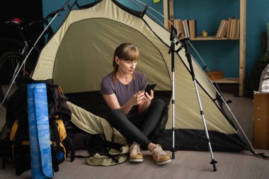 Orta yaşlı bir kadın çadırın yanında oturmuş evdeki akıllı telefonu kullanıyor. Turist aktif bir hayat sürüyor. Yürüyüş, seyahat ve gezi konsepti