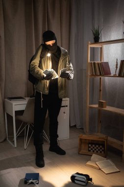 Burglar or intruder with flashlight. Illegally breaking. Male robber wearing black balaclava steals money from apartment. Thief committing theft. Criminal offence. burglary and housebreaking concept