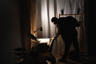 Burglar or intruder with flashlight. Illegally breaking. Male robber wearing black balaclava steals money from apartment. Thief committing theft. Criminal offence. burglary and housebreaking concept