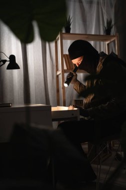 Illegally breaking. Male robber wearing black balaclava steals money from desk at apartment. Thief committing theft. Criminal offence. burglary, housebreaker. copy space