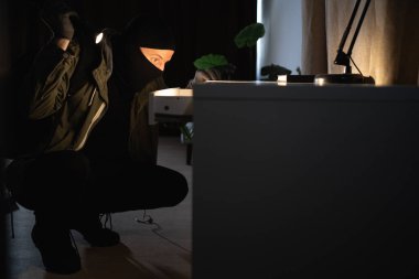 Illegally breaking. Male robber wearing black balaclava steals money from desk at apartment. Thief committing theft. Criminal offence. burglary, housebreaker. Copy space