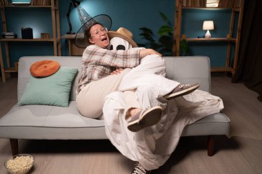 scary scene. Man horror ghost sitting on sofa holding woman on his knees watching thriller movie, hugging each other. copy space